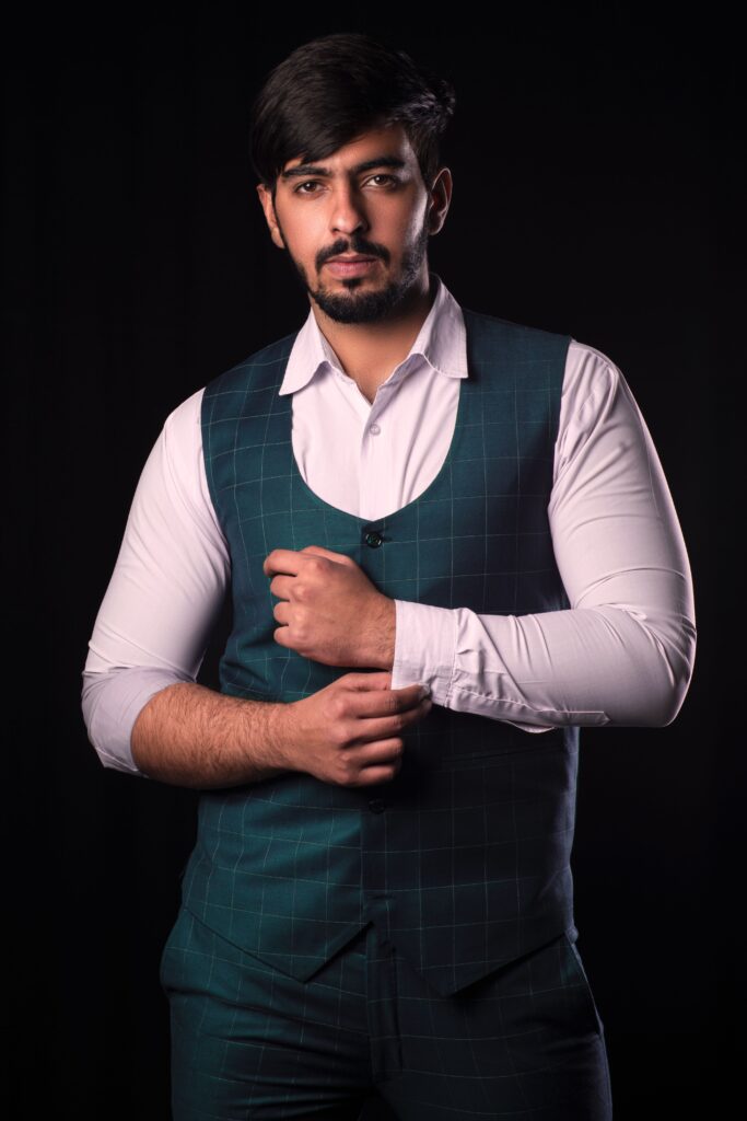 Portrait of a confident South Asian man in a stylish vest and shirt, posing in a studio setting.