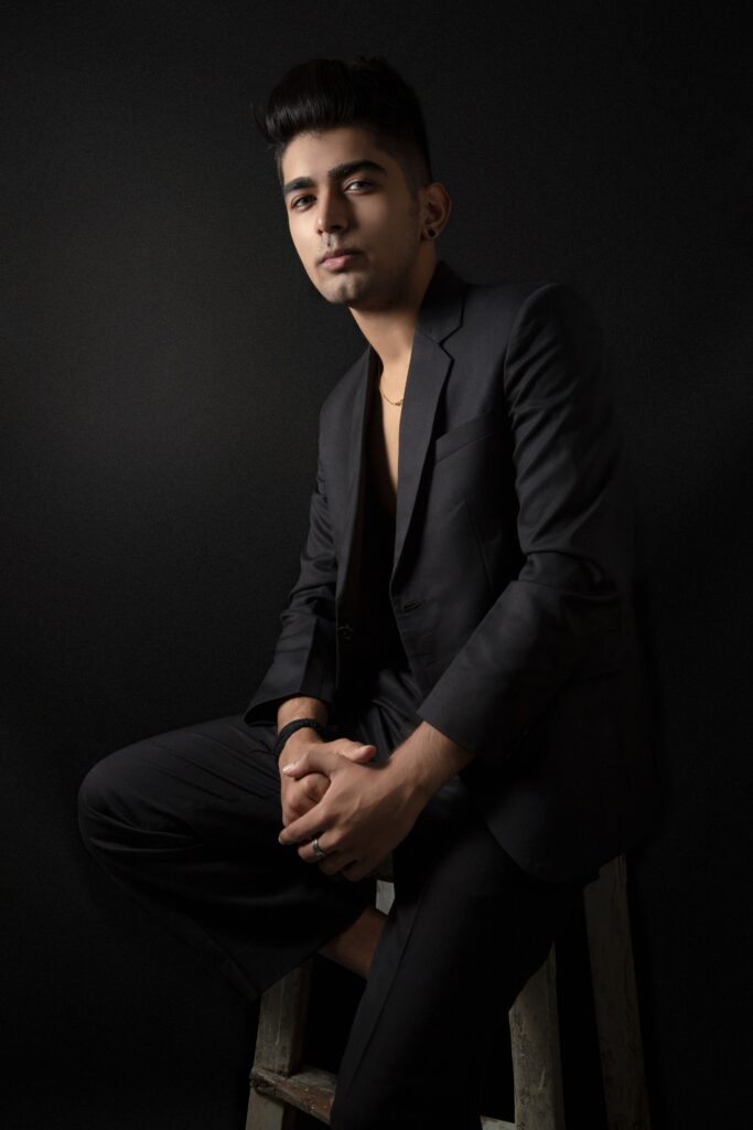 Studio portrait of a man in a black suit, sitting against a black background, conveying a professional and elegant vibe.